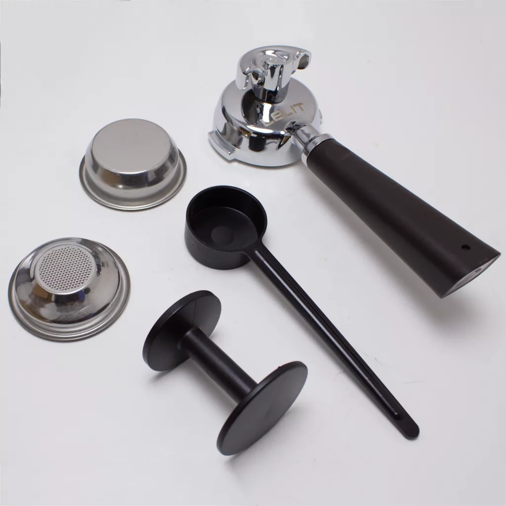 A coffee portafilter with a black handle, two metal filter baskets, a black plastic scoop, a tamper, and a metal filter screen are arranged on a white surface. © 2025 1st-line.com