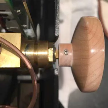 Close-up view of a wooden knob attached to a brass fitting, with a copper tube and metal components nearby, possibly part of an Ascaso Dream PID steam wand tip on a mechanical or scientific device. © 2025 1st-line.com