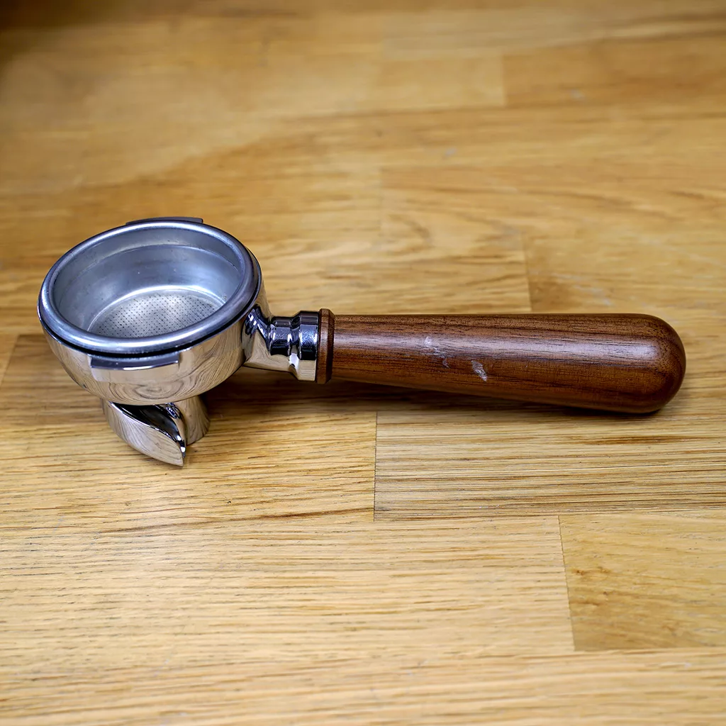 A metal espresso portafilter with a wooden handle rests on a light wood surface, ready for use with the (SOLD) SIDEWALK SALE - Lelit PL60PLUST Diana Espresso Machine. © 2025 1st-line.com