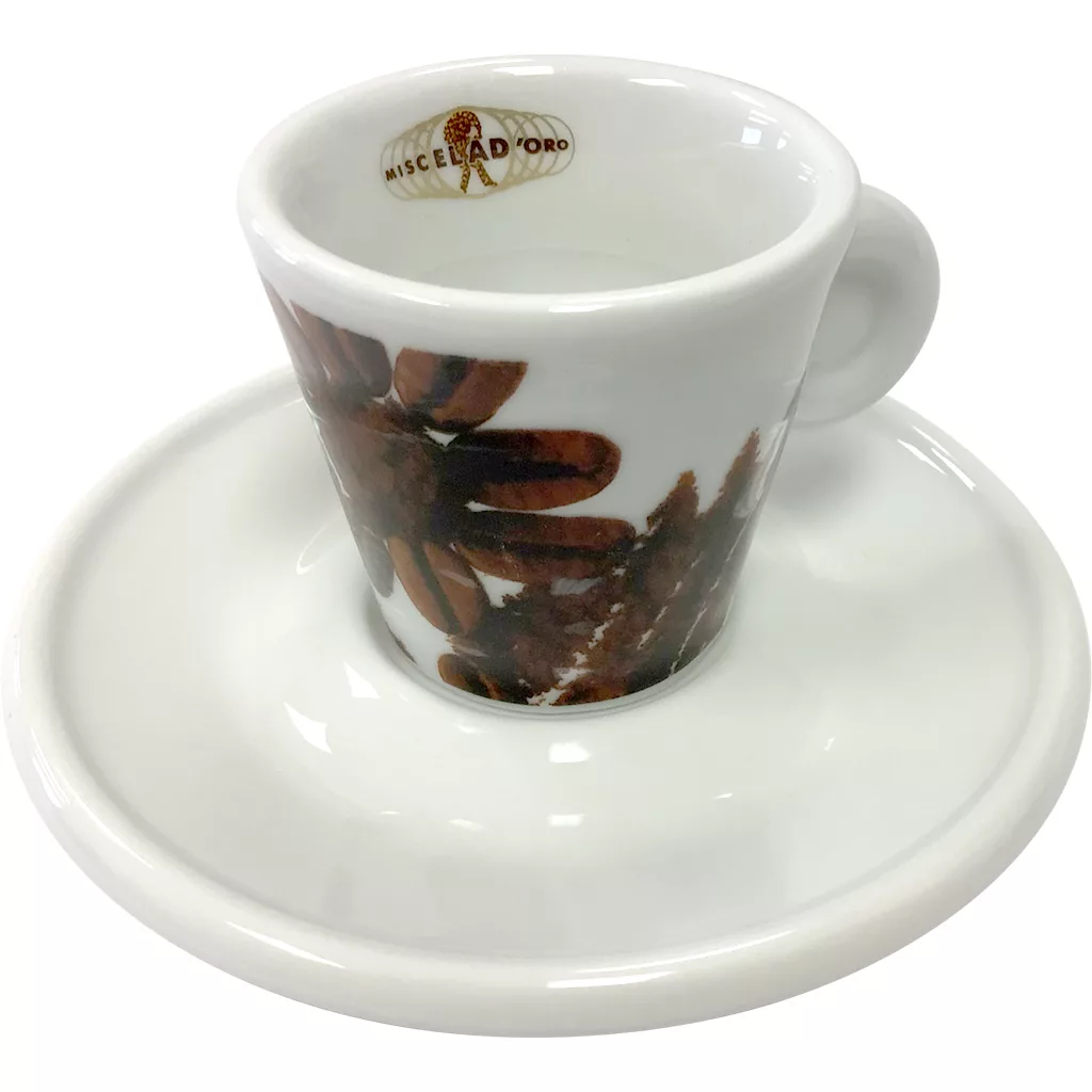 A white porcelain Espresso cup with a brown floral design and the gold Miscela d’Oro logo sits elegantly on a matching white saucer. © 2025 1st-line.com