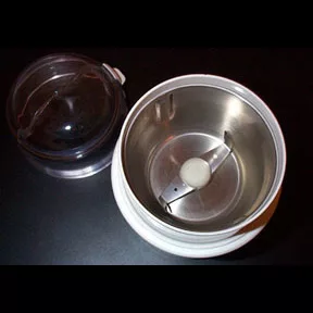 Top view of an open blade grinder coffee grinder showing its metal blades and lid placed beside it on a dark surface—a great way to explore blade vs burr grinding. © 2025 1st-line.com