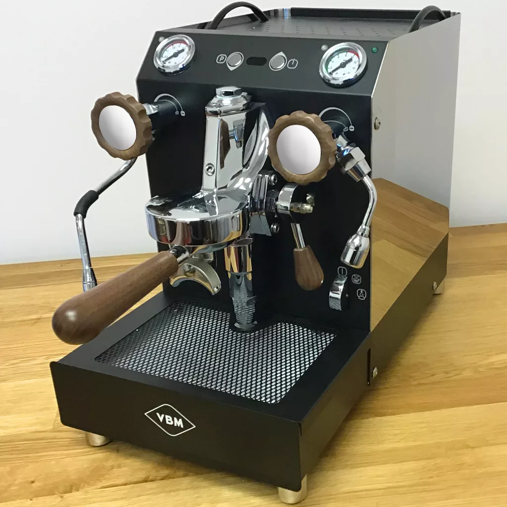 A VBM espresso machine featuring the Walnut Wood Kit—knobs and portafilter handle—sits ready on a wooden countertop, combining elegant walnut accents with dual gauges for brewing coffee. © 2025 1st-line.com