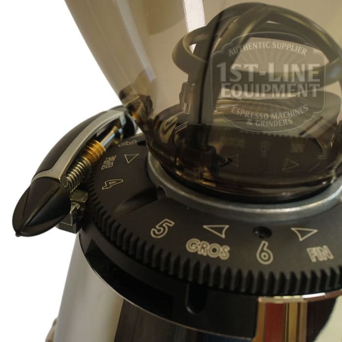 Close-up of an Elektra MXD Maxi Digital Espresso Coffee Grinder displaying its numbered grind size adjustment dial, clear top hopper, and a reflection of the 1st-Line Equipment logo on the hopper. © 2025 1st-line.com