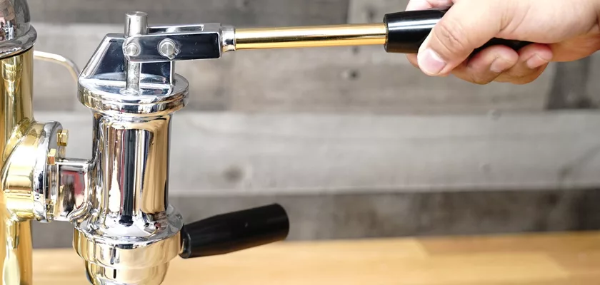A hand grips the lever of the shiny Elektra Microcasa a Leva Espresso Machine, set against a wooden background and ready to pull a rich shot of espresso. © 2025 1st-line.com