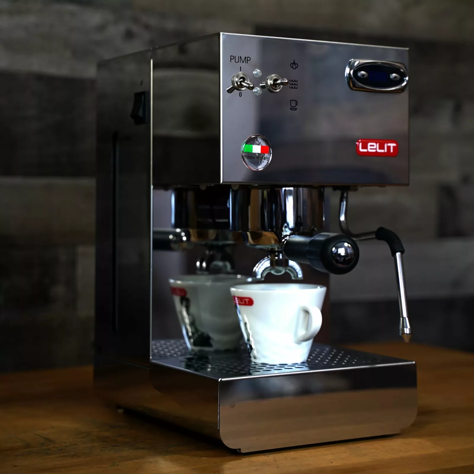 A stainless steel DISCONTINUED Lelit Glenda PL41PLUST PID Espresso & Cappuccino Machine sits on a wooden counter, brewing coffee into a white cup. The machine features a steam wand and labeled buttons on its front panel. © 2025 1st-line.com