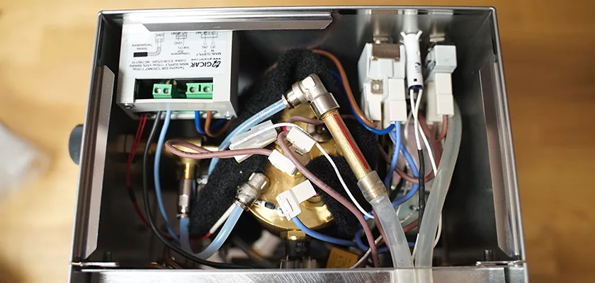 Top-down view of the internal components of the DISCONTINUED Lelit Glenda PL41PLUST PID Espresso & Cappuccino Machine, showing neatly arranged wires, metal pipes, connectors, a relay module, and a brass fitting inside the metal casing. © 2025 1st-line.com