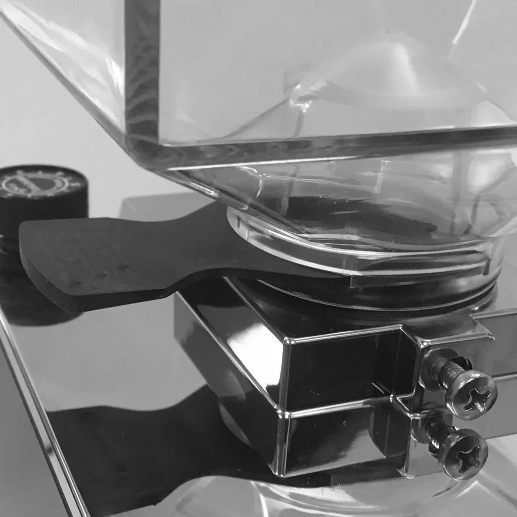 A close-up, black-and-white photo of a mechanical device with metal screws, burrs, a reflective surface, and a transparent container on top; possibly part of an Eureka Mignon Grinder or kitchen scale. © 2025 1st-line.com