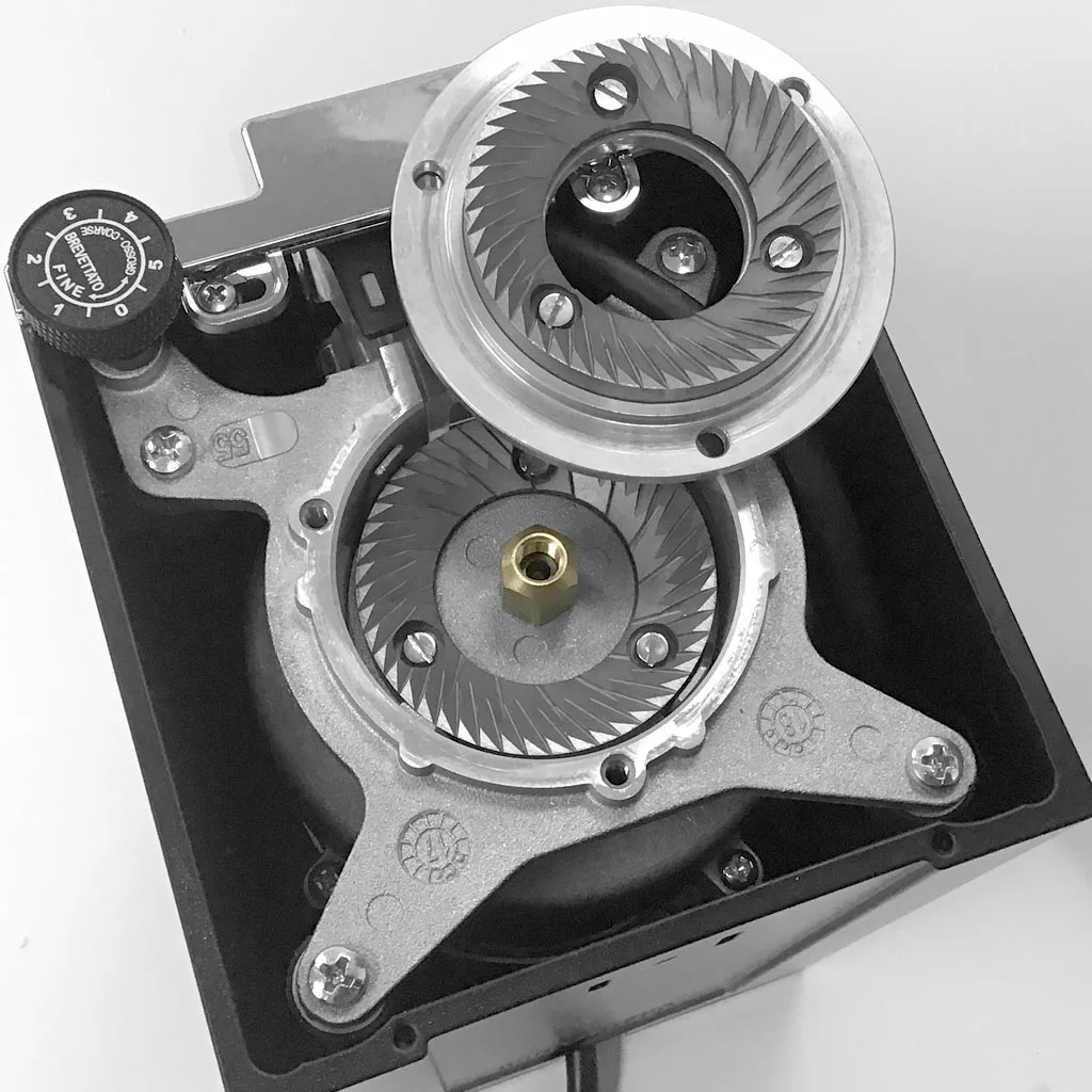 Black and white photo of an open Eureka Mignon Grinder, showing the sharp burrs access, adjustment dial, and internal mechanical components. © 2025 1st-line.com