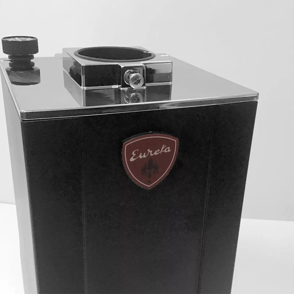 Close-up of a black and silver Eureka Mignon Grinder with a red “Eureka” logo and round opening on top for accessing the burrs, set against a plain white background. © 2025 1st-line.com