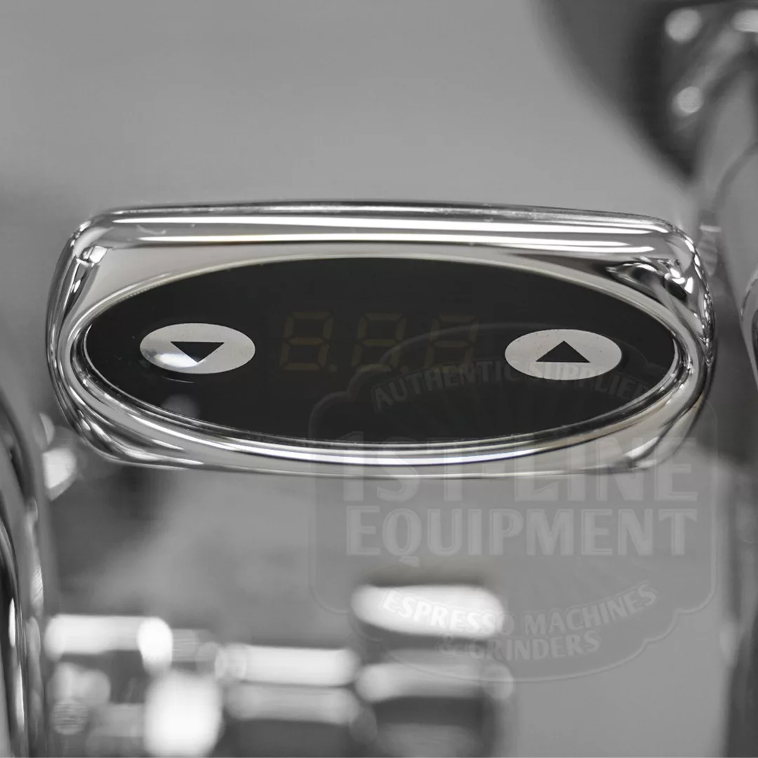 A close-up of a digital control panel with arrow buttons and a dark display foregrounds the discontinued Izzo Valexia Duetto II Dual Boiler Espresso Machine, with “1st Line Equipment” text blurred in the background. © 2025 1st-line.com