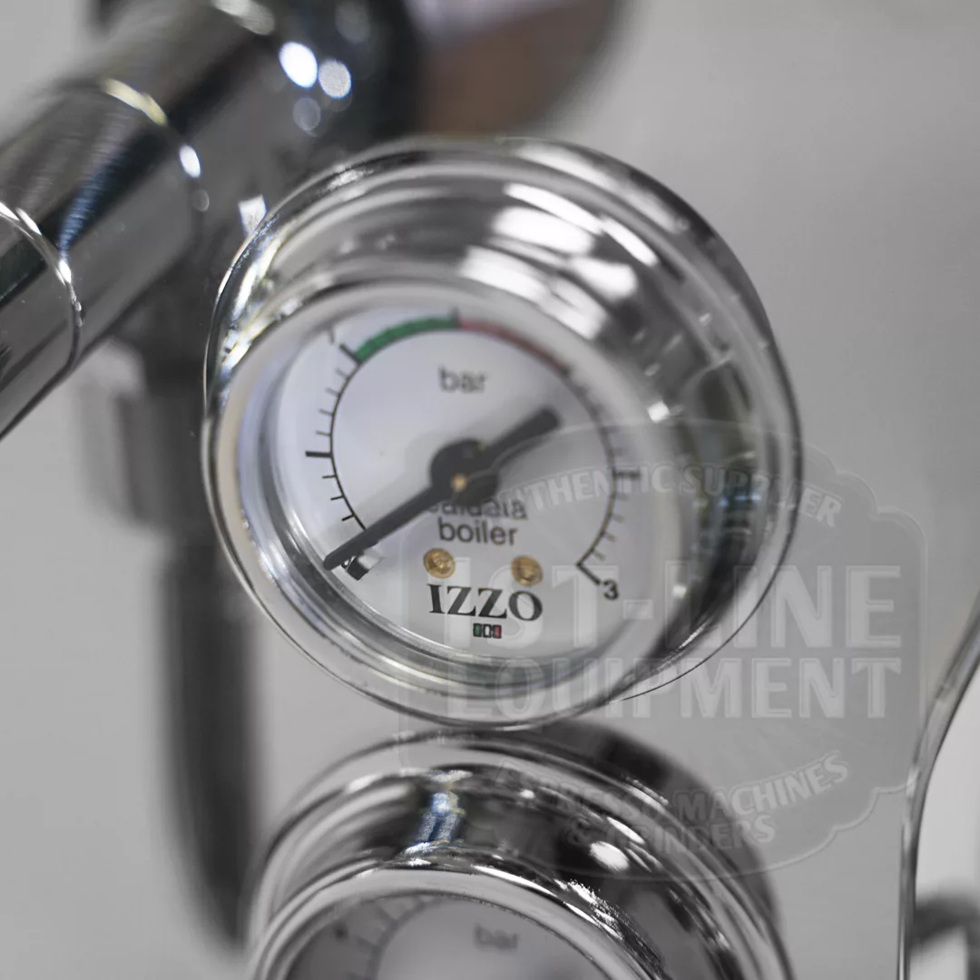 A close-up of a shiny metal pressure gauge on an espresso machine, displaying measurements in bars. The gauge reads boiler and IZZO, with a needle pointing to just under 1 bar. © 2025 1st-line.com