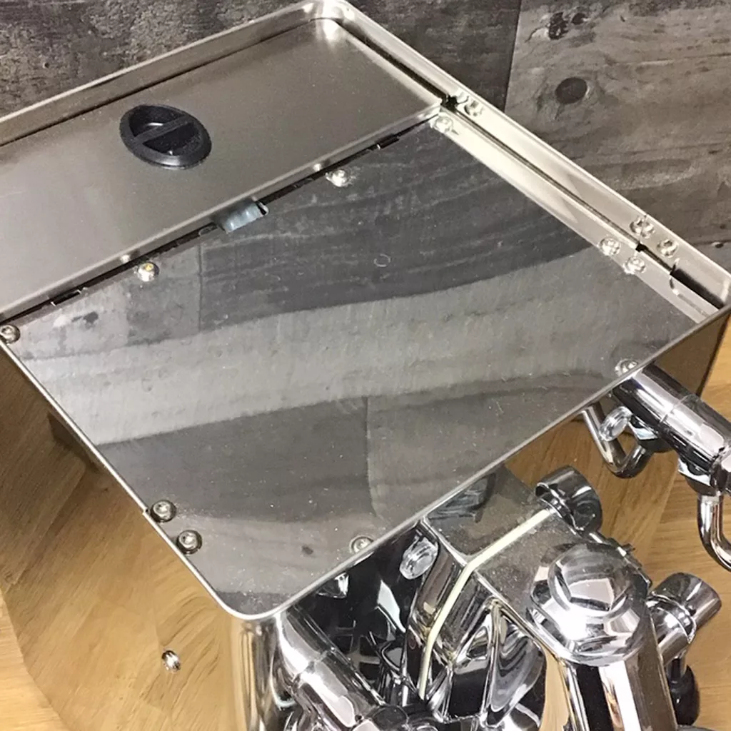 A close-up of a shiny, returned & refurbished Lelit PL62 Mara Heat Exchange Espresso Machine (SOLD IN STORE PICKUP), highlighting the top with removable lid and black knob, reflecting wooden flooring and a tiled wall. © 2025 1st-line.com