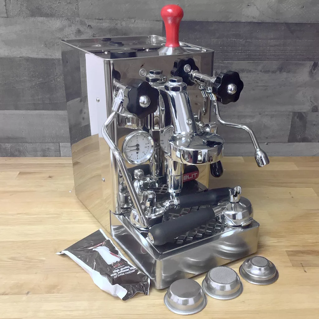 A refurbished Lelit PL62 Mara Heat Exchange Espresso Machine (SOLD IN STORE PICKUP) sits on a wooden surface with metal filter baskets and a packet, set against a gray tiled wall. © 2025 1st-line.com
