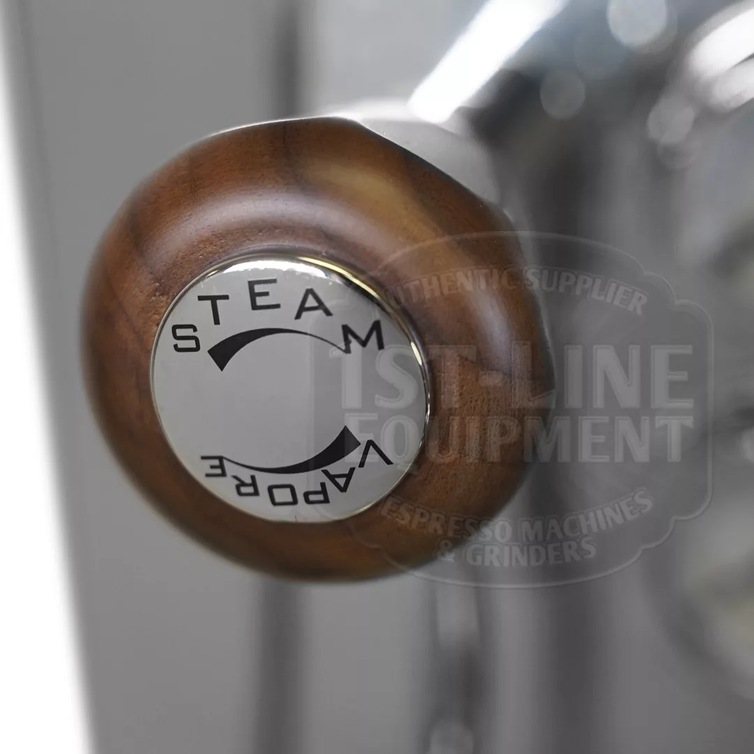 Close-up of a wooden steam control knob with a metal cap labeled STEAM and VAPORE, featuring directional arrows, on the DISCONTINUED Izzo Valexia Duetto II Dual Boiler Espresso Machine. Blurred branding appears in the background. © 2025 1st-line.com