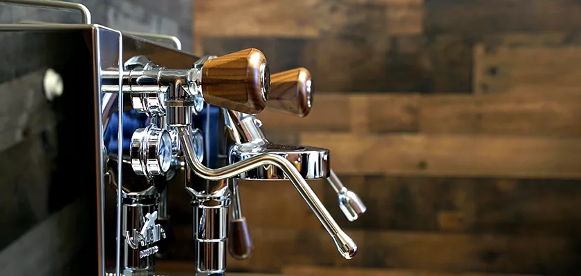 Close-up of the DISCONTINUED Izzo Valexia Duetto II Dual Boiler Espresso Machine with wooden handles and metal levers, set against a backdrop of wooden wall panels. © 2025 1st-line.com