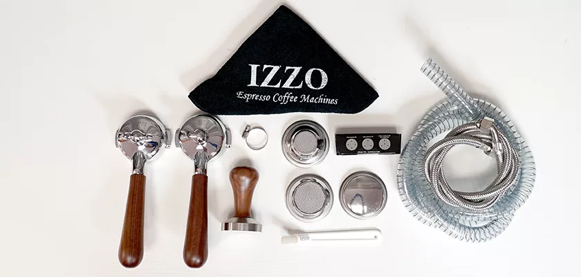 Various espresso machine accessories, such as two portafilters, a black IZZO towel, and tools for the DISCONTINUED Izzo Valexia Duetto II Dual Boiler Espresso Machine, are neatly arranged on a white surface. © 2025 1st-line.com