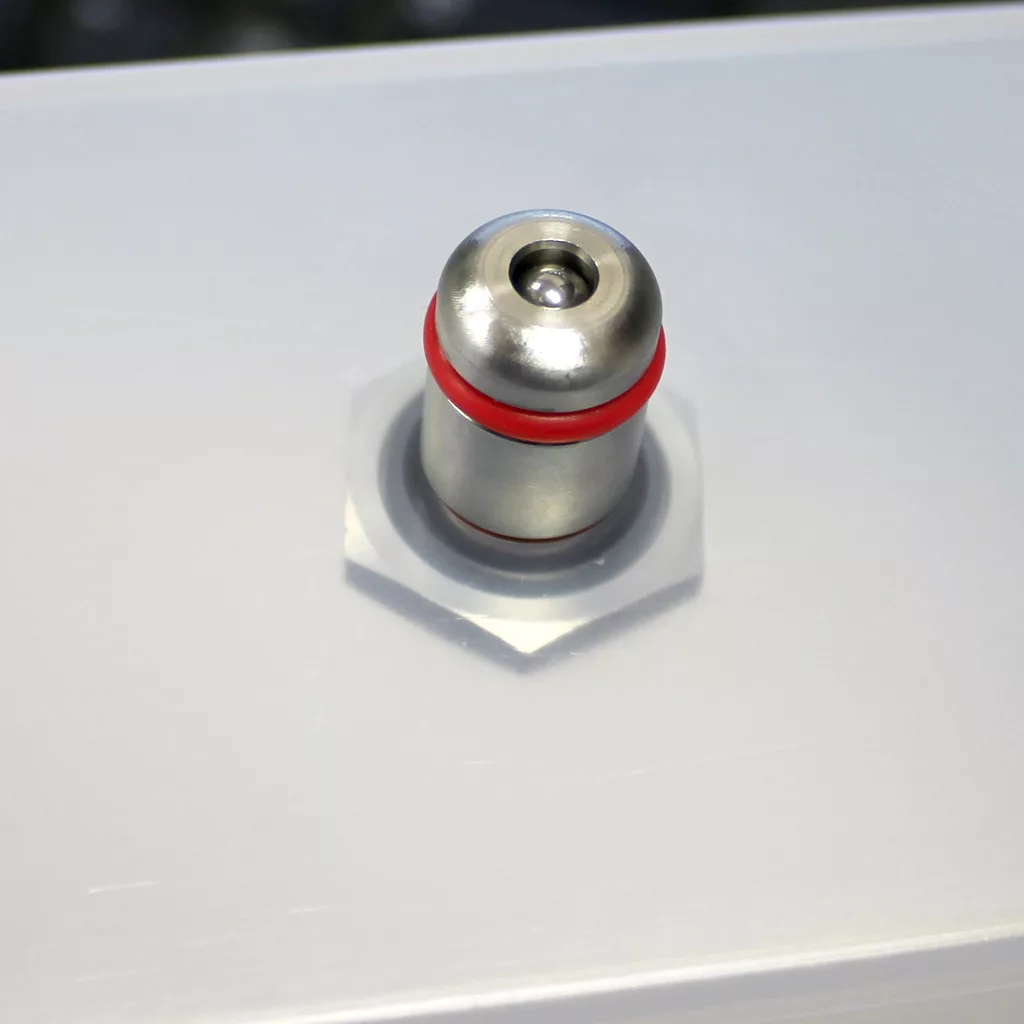 A close-up of a stainless steel nozzle with a red O-ring, mounted on a smooth, light gray surface. The nozzle is centered within a hexagonal fitting—ideal for installing ECM Switchable models or as a water tank adapter. © 2025 1st-line.com