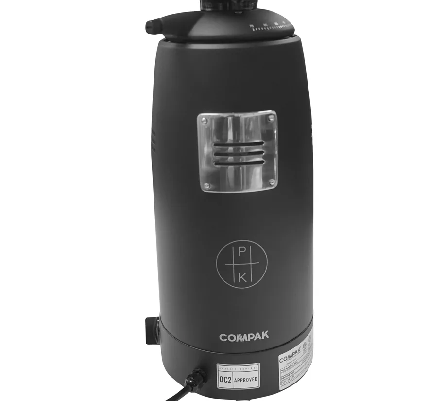 A discontinued Compak PKE Stepless Doserless Espresso Coffee Grinder in matte black, shown from the back with a silver vent, plug-in power cord, visible PK logo, and certification labels on the lower part of the machine. © 2025 1st-line.com