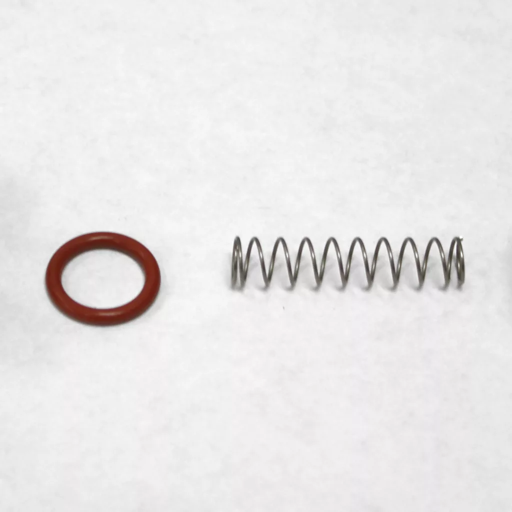 A metal coil spring and a red rubber O-ring, ideal for water tank adapter installation, are placed side by side on a white surface. © 2025 1st-line.com