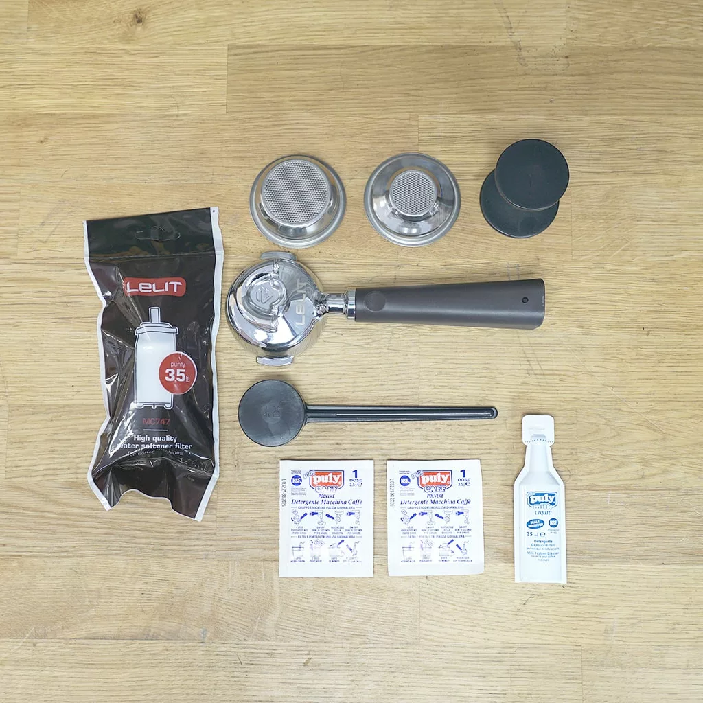 Accessories for the (SOLD) SIDEWALK SALE - Lelit PL92T Elizabeth PID Version 3 Dual Boiler Espresso Machine include a portafilter, two filter baskets, black tampers, Lelit water filter, cleaning powder sachets, brush, and cleaning fluid. © 2025 1st-line.com