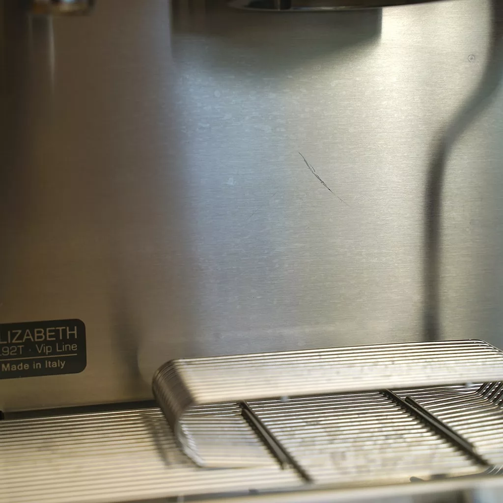 Close-up of a stainless steel Lelit PL92T Elizabeth PID V3 Dual Boiler Espresso Machine (RETURNED & REFURBISHED), showing a scratch, drip tray, and part of the label—model E211. © 2025 1st-line.com