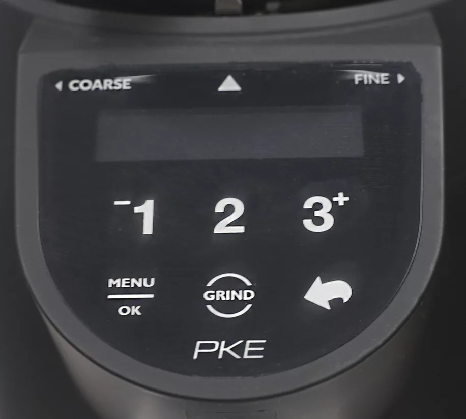 Close-up of the DISCONTINUED Compak PKE Stepless Doserless Espresso Coffee Grinder in Matte Black, highlighting its control panel with a digital screen, buttons 1, 2, 3+, MENU OK, GRIND, a return arrow, and stepless grind adjustment. © 2025 1st-line.com