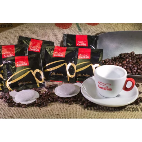 Five packets of DISCONTINUED Caffe Castorino Gold Arabica E.S.E. Pods (100/case), a white espresso cup and saucer, coffee beans, and a metal scoop are artfully displayed on a burlap sack. © 2025 1st-line.com