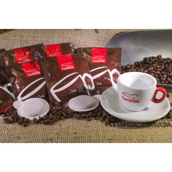 Packets of DISCONTINUED Caffe Castorino Forte E.S.E. Pods - 100/case, a white espresso cup and saucer with the Castorino logo, two pods, and coffee beans sit on a rustic burlap surface. © 2025 1st-line.com