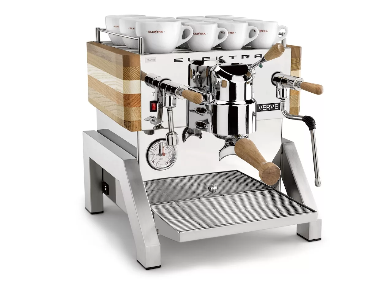 The Elektra Verve Dual Boiler Espresso Machine features a polished chrome finish, wooden handles and side panels, a top cup rack with white cups, and a front pressure gauge showcasing its dual boiler performance. © 2025 1st-line.com