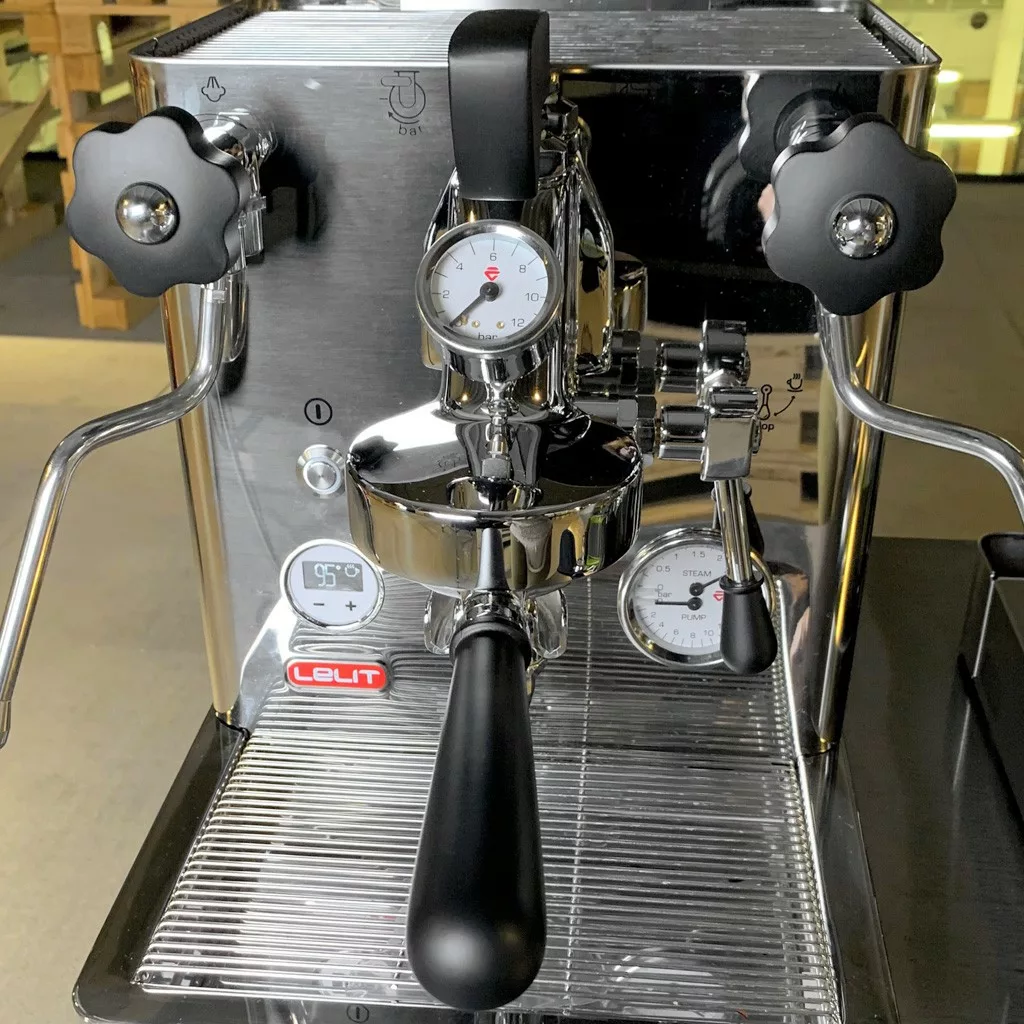 A close-up of a shiny stainless steel Lelit espresso machine with two pressure gauges, side steaming wands, and a central portafilter handle. The Lelit PLA2201 Black Wood Kit beautifully accents the front panel. © 2025 1st-line.com