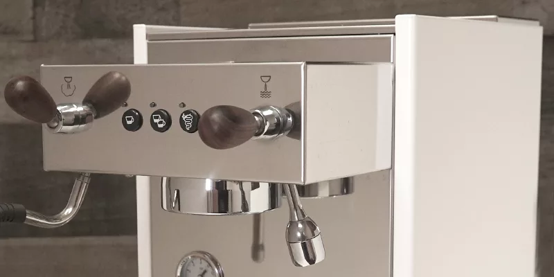 A close-up of the Bezzera Crema DE HX Espresso Machine, featuring wooden handles, a metallic finish, black control buttons, a steam wand, and a pressure gauge against a neutral background. © 2025 1st-line.com