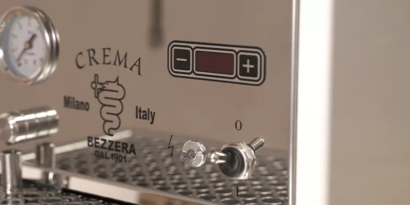 A close-up of the Bezzera Crema DE HX Espresso Machine highlights its pressure gauge, control buttons, indicator lights, and Milano Italy branding on a sleek stainless steel front panel. © 2025 1st-line.com