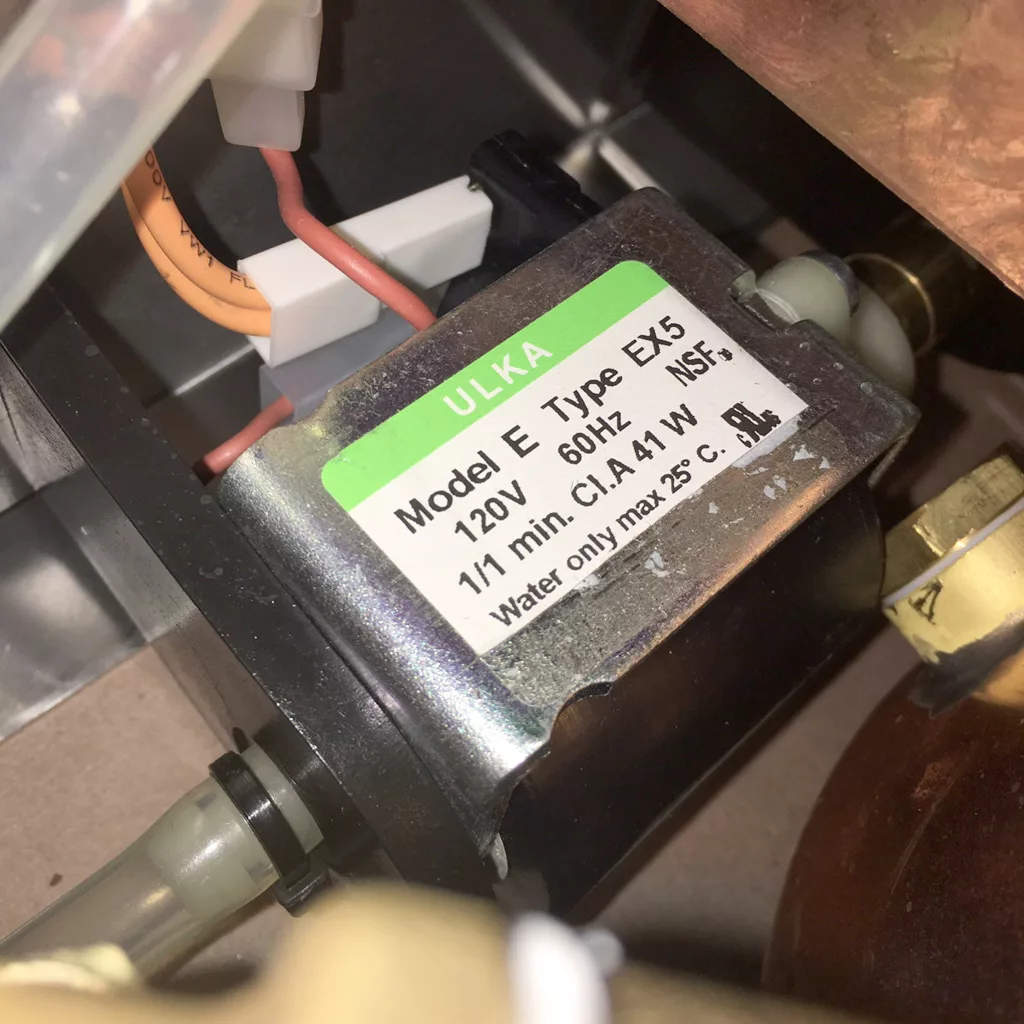 Close-up of an electric pump labeled ULKA Model E Type EX5, 120V, 60Hz, used in a VBM Super HX espresso machine. Various wires and tubes are connected; labeled for water only up to 25°C and intended for tank only setups. © 2025 1st-line.com