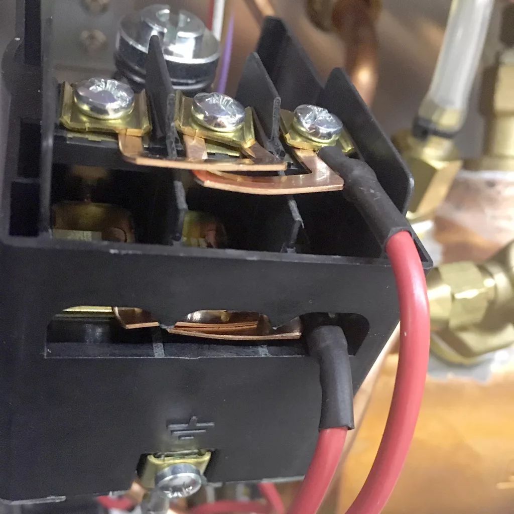 Close-up of an electrical relay with red and black wires connected to terminals, copper contacts, and screws visible, set against a background with brass fittings and tubing inside a VBM Super HX espresso machine. © 2025 1st-line.com