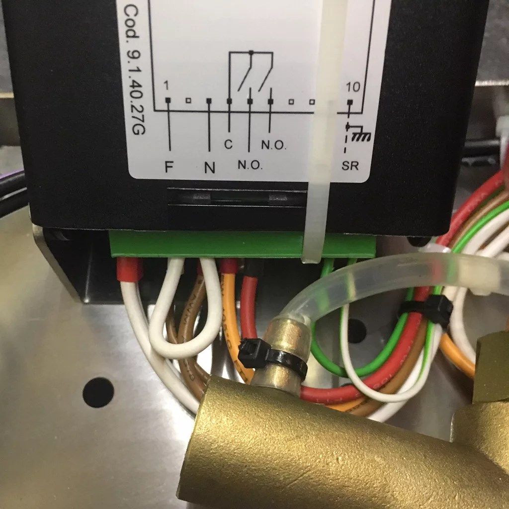 Close-up of electrical wiring connected to a black device with a circuit diagram and label Cod. 91.4027G on top; various colored wires are attached below, next to a brass component and clear tube in a VBM Super HX espresso machine. © 2025 1st-line.com