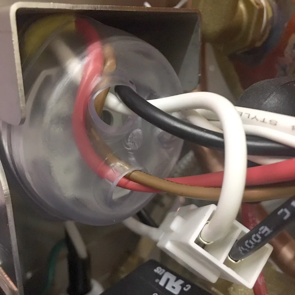 Close-up of electrical wiring inside an espresso machine, connected to a transparent circular component. Red, black, brown, and white wires are visible—typical of internal components found in a VBM Super HX tank only model. © 2025 1st-line.com