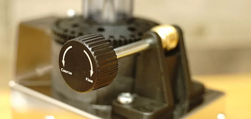 Close-up of the black adjustment knob on the DISCONTINUED Lelit PL043MMI Fred Espresso Coffee Grinder, showing white arrows for Coarse and Fine grind settings, attached to a metal rod for grind size control. © 2025 1st-line.com