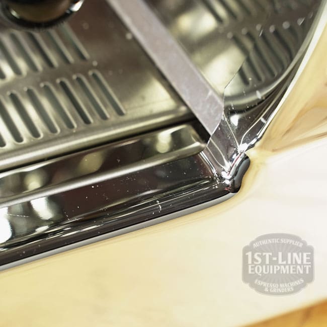 Close-up of the Like NEW- La Nuova Era Cuadra Espresso Machine - V3 Chrome (C105) corner shows a visible weld, reflective chrome surface, and a partially visible 1st-Line Equipment logo, highlighting its quality design. © 2025 1st-line.com