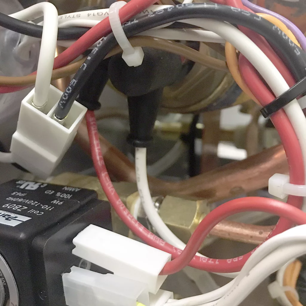 Close-up of various electrical wires, connectors, and cables in different colors secured with zip ties inside a VBM Super HX espresso machine, showing detailed components and copper tubing. © 2025 1st-line.com