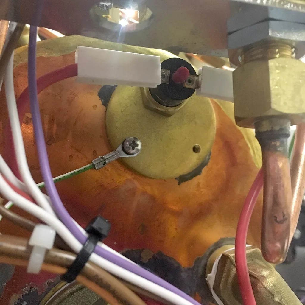 Close-up view of a VBM Super HX espresso machine’s mechanical assembly, featuring wires, a brass fitting, screws, and a copper surface with heat discoloration. White and purple cables are bundled with a zip tie in the foreground. © 2025 1st-line.com