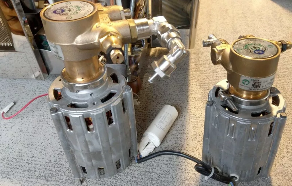 Two metallic Rotary Vane Pumps with gold-colored tops and cylindrical silver bases are placed on a speckled surface. One 150-watt pump has attached pipes, and wires are visible near both bases. © 2025 1st-line.com