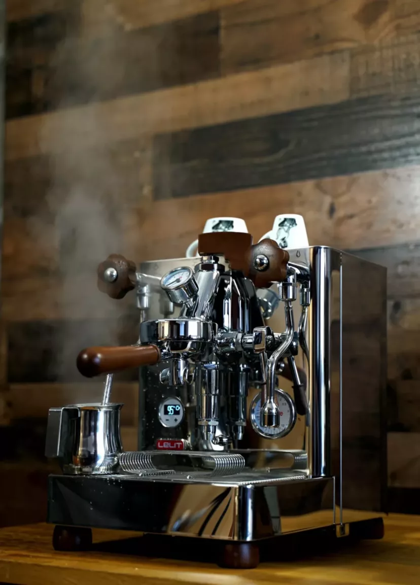 A (SOLD) SIDEWALK SALE - Lelit Bianca Dual Boiler Espresso Machine V2 PID w/ Manual Brew Pressure Profiling DEMO MODEL sits on a wooden counter, steam curling from its spout beside a metal milk pitcher, against a rustic wood-paneled wall. © 2025 1st-line.com