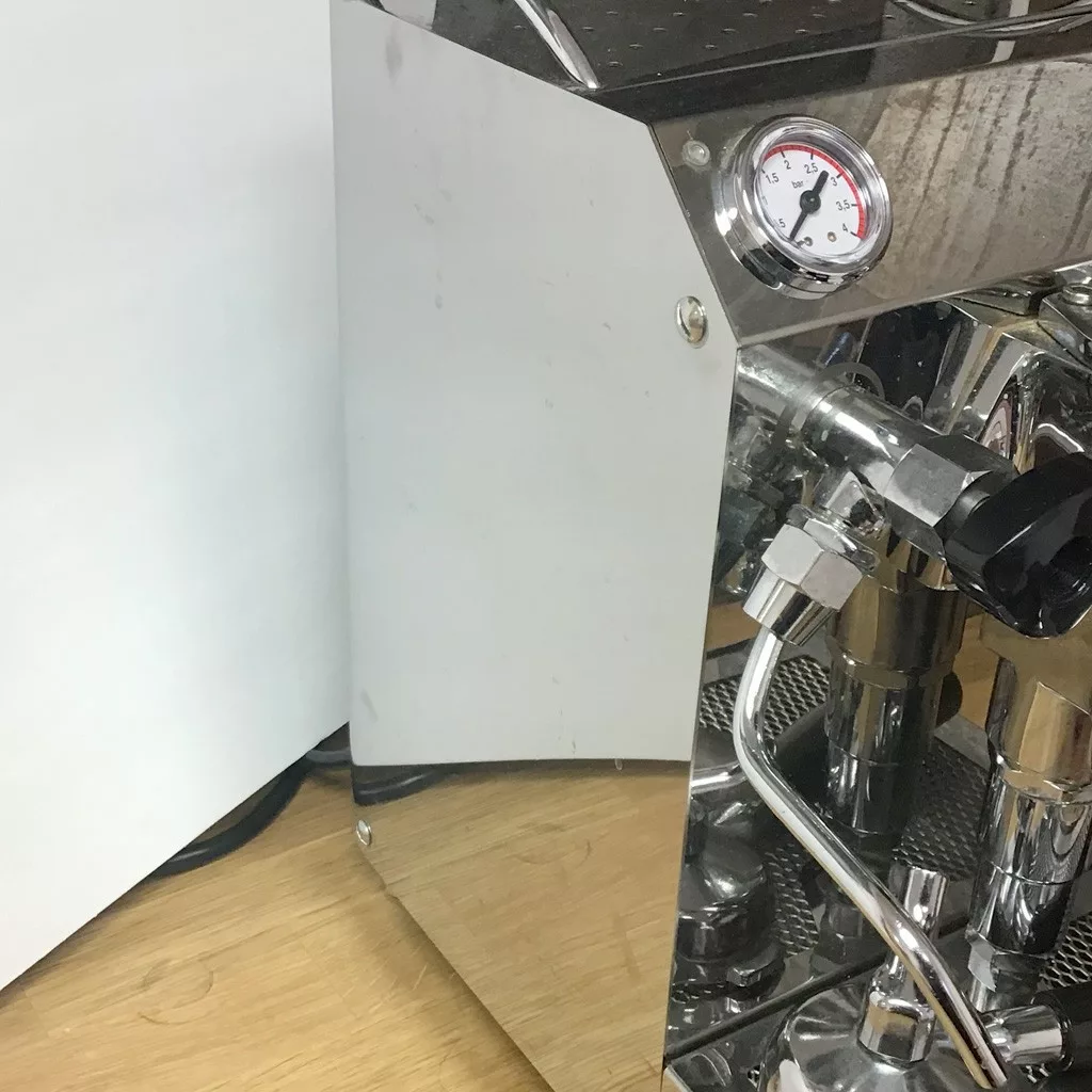 A detailed view of the SOLD SIDEWALK SALE VBM Domobar Junior HX Espresso Machine shows its pressure gauge, steam wand, and polished reflections while it sits on a wooden countertop. © 2025 1st-line.com