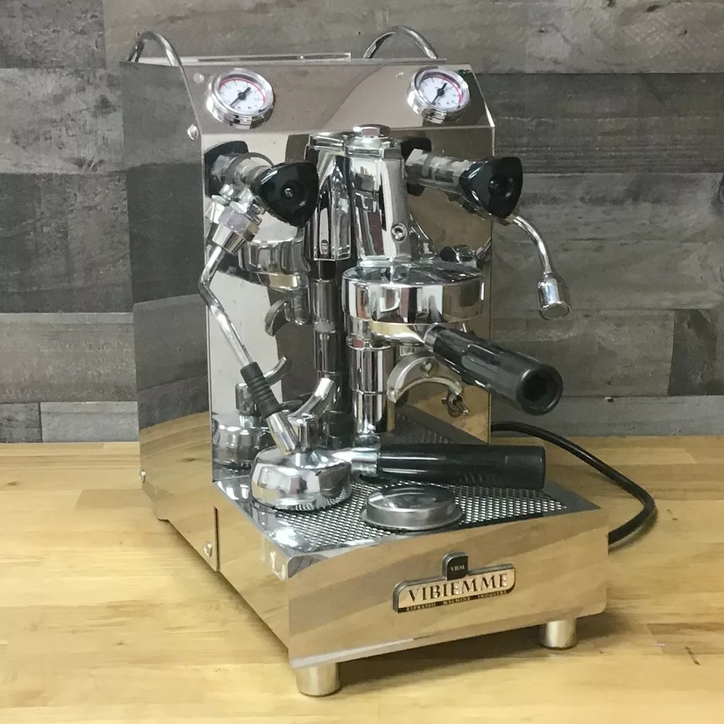 A SOLD SIDEWALK SALE VBM Domobar Junior HX Espresso Machine with two pressure gauges, stainless steel body, multiple levers, and a steam wand sits on a wooden countertop. The front displays the Vibiemme brand name. © 2025 1st-line.com