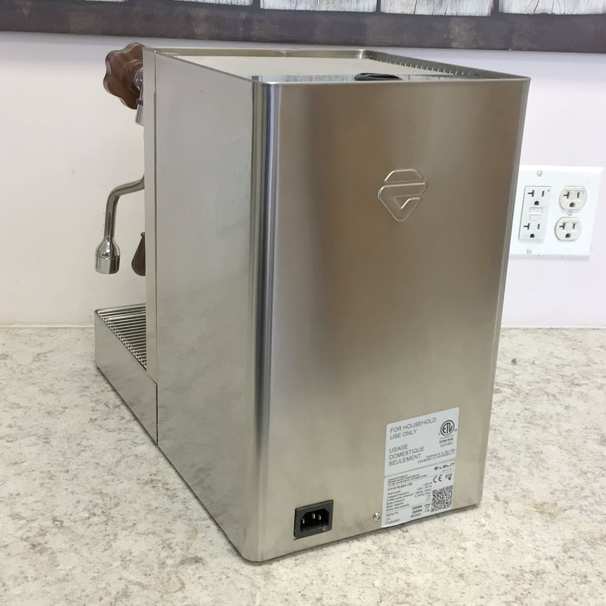 A SIDEWALK SALE - Lelit Mara X PL62X HX Espresso Machine (used) (E213) with a stainless steel body and wooden handle is pictured from the back and side on a light countertop near a wall with outlets. © 2025 1st-line.com