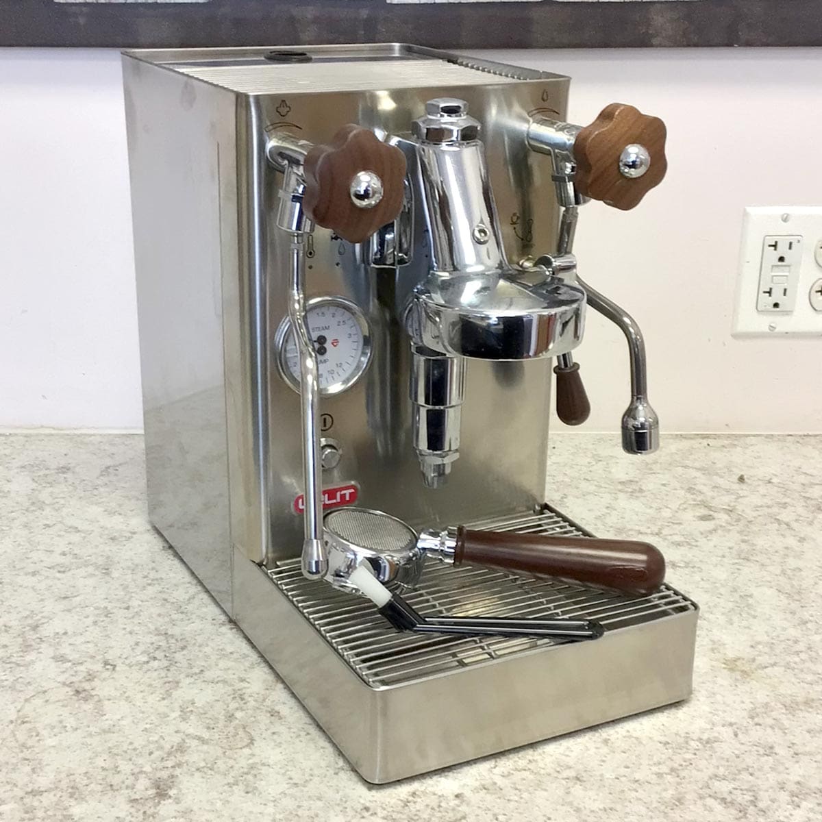 A used SIDEWALK SALE - Lelit Mara X PL62X HX Espresso Machine (E213) with wooden handles sits on a countertop. A portafilter and tamper are on the drip tray; a pressure gauge, steam wand, and nearby outlet are also visible. © 2025 1st-line.com