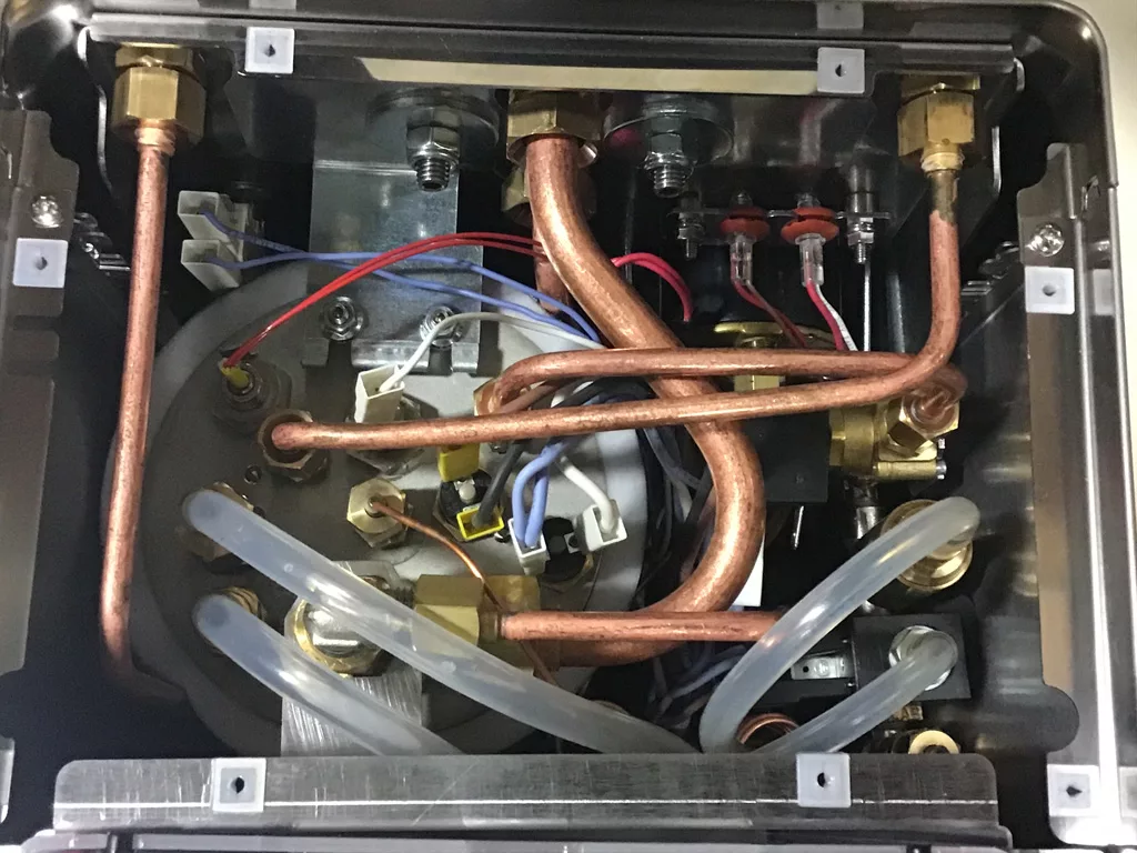 Close-up view of the inside of a Lelit Mara X machine, highlighting copper pipes, wires, clear plastic tubes, and metal fittings arranged in a compact layout—perfect for understanding repair or water tank connection details. © 2025 1st-line.com