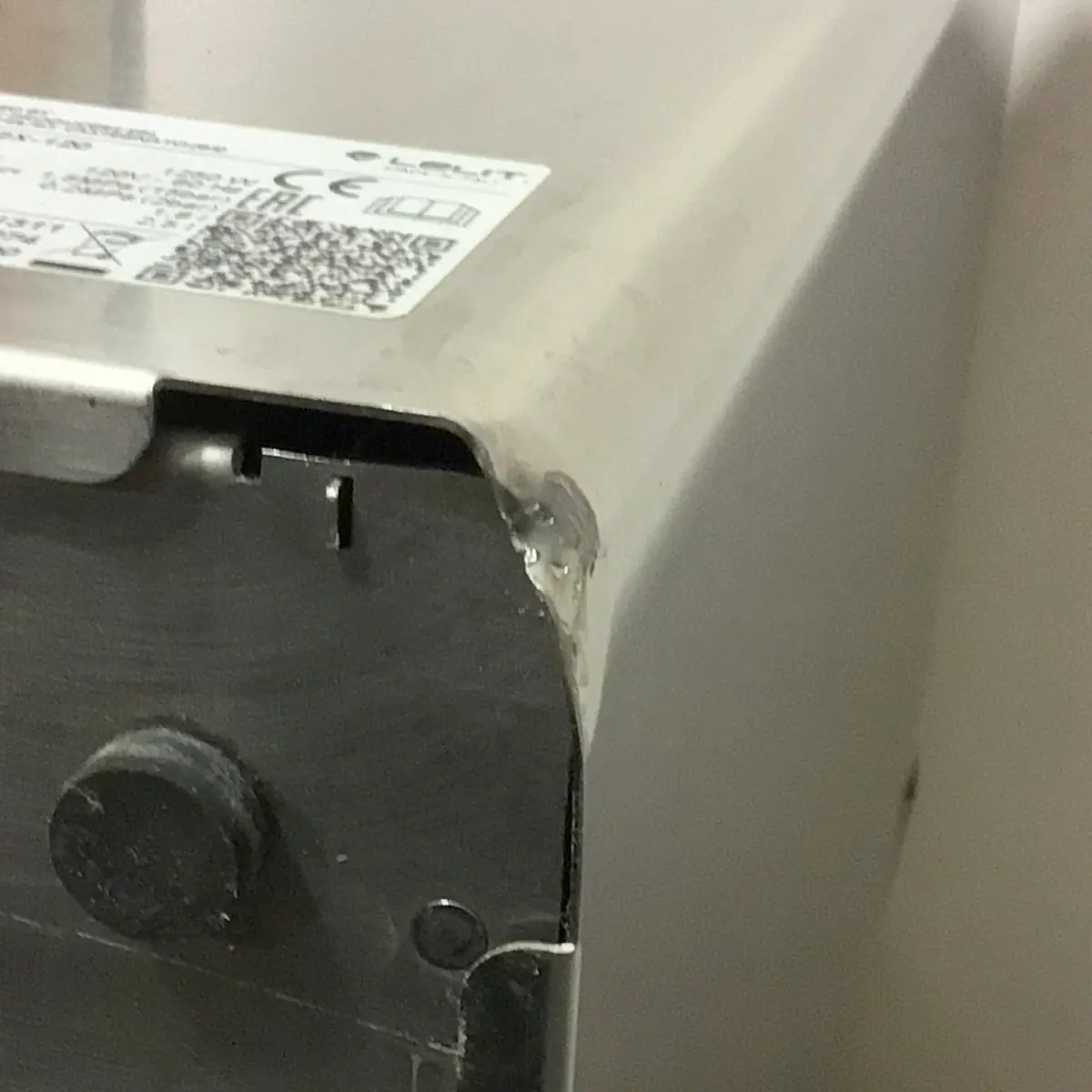 Close-up of a used SOLD SIDEWALK SALE - Lelit Mara X PL62X HX Espresso Machine (E213), showing a dented and chipped corner. A label with a QR code and symbols is partially visible on the top surface.