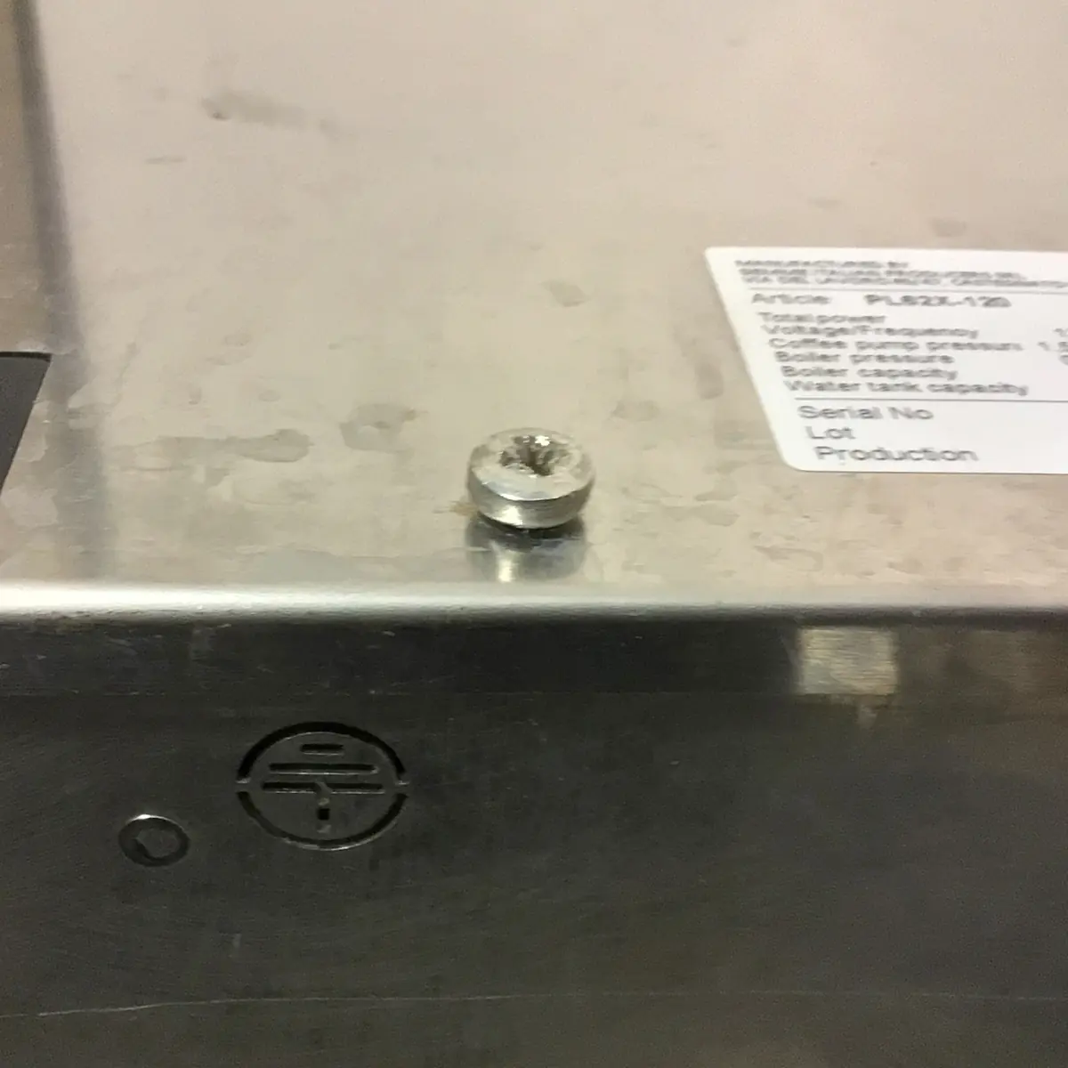 A flat, silver screw with a stripped Phillips head is set in a metal surface near a sticker label and the circular logo of the SOLD SIDEWALK SALE - Lelit Mara X PL62X HX Espresso Machine (used) (E213).