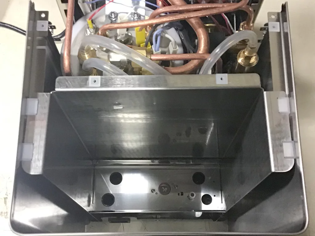 Top-down view of the inside of a Lelit Mara X, showing various copper pipes, wires, transparent tubes, and an empty rectangular steel compartment near the water tank connection, ideal for repair or maintenance insights. © 2025 1st-line.com